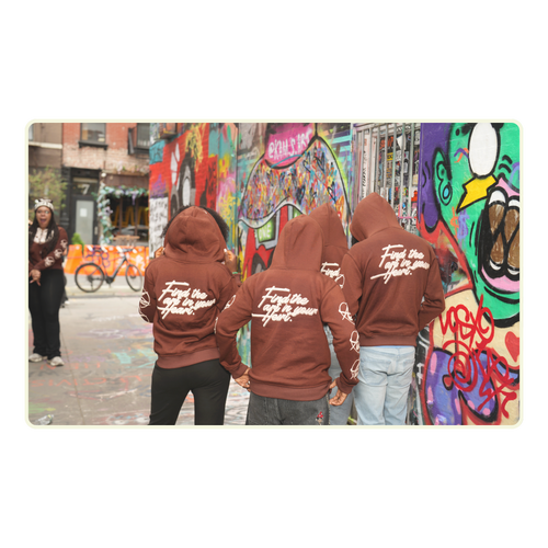 Three people wearing brown hoodies with text, standing in front of a colorful graffiti wall.
