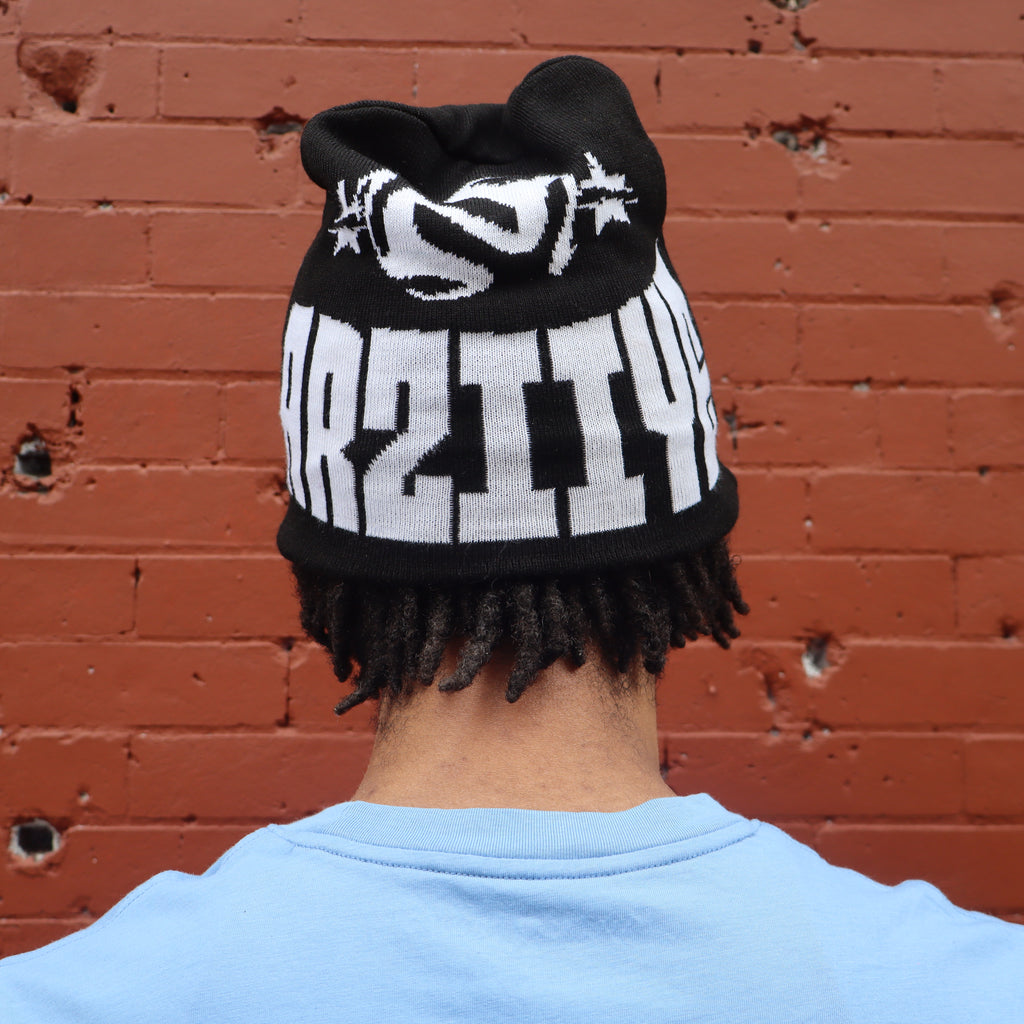 Person wearing a black and white beanie with text against a red brick wall