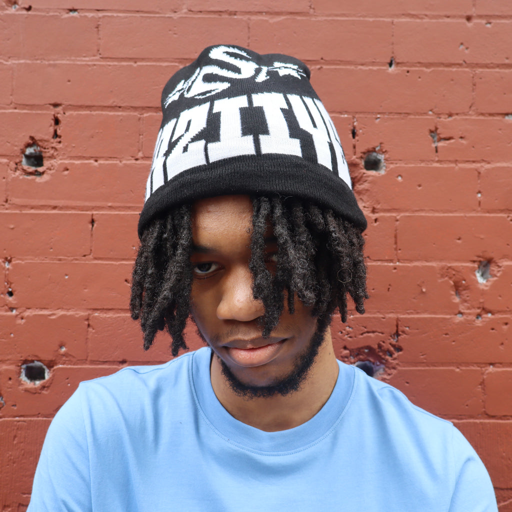 Person wearing a black and white beanie with text against a red brick wall