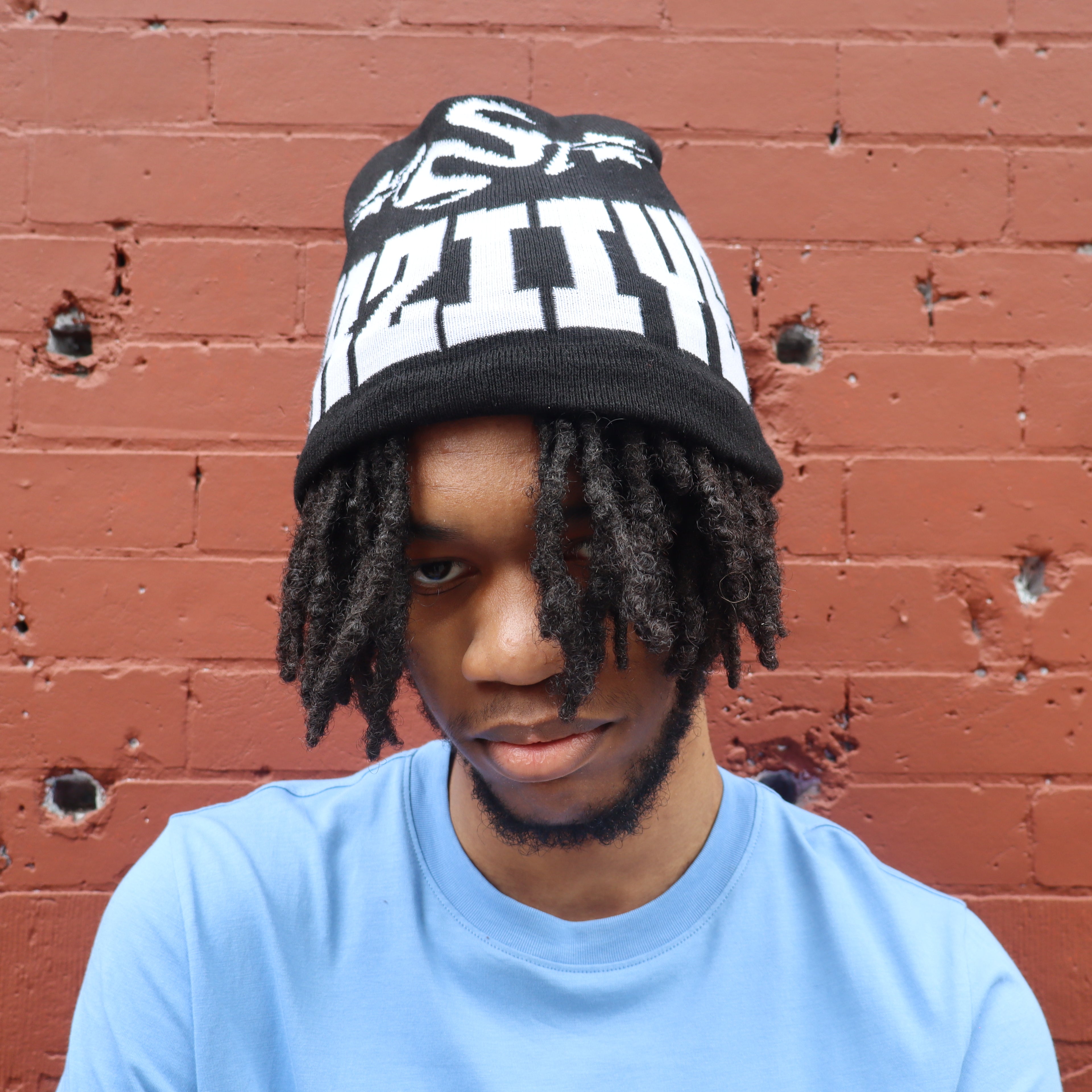 Person wearing a black and white beanie with text against a red brick wall