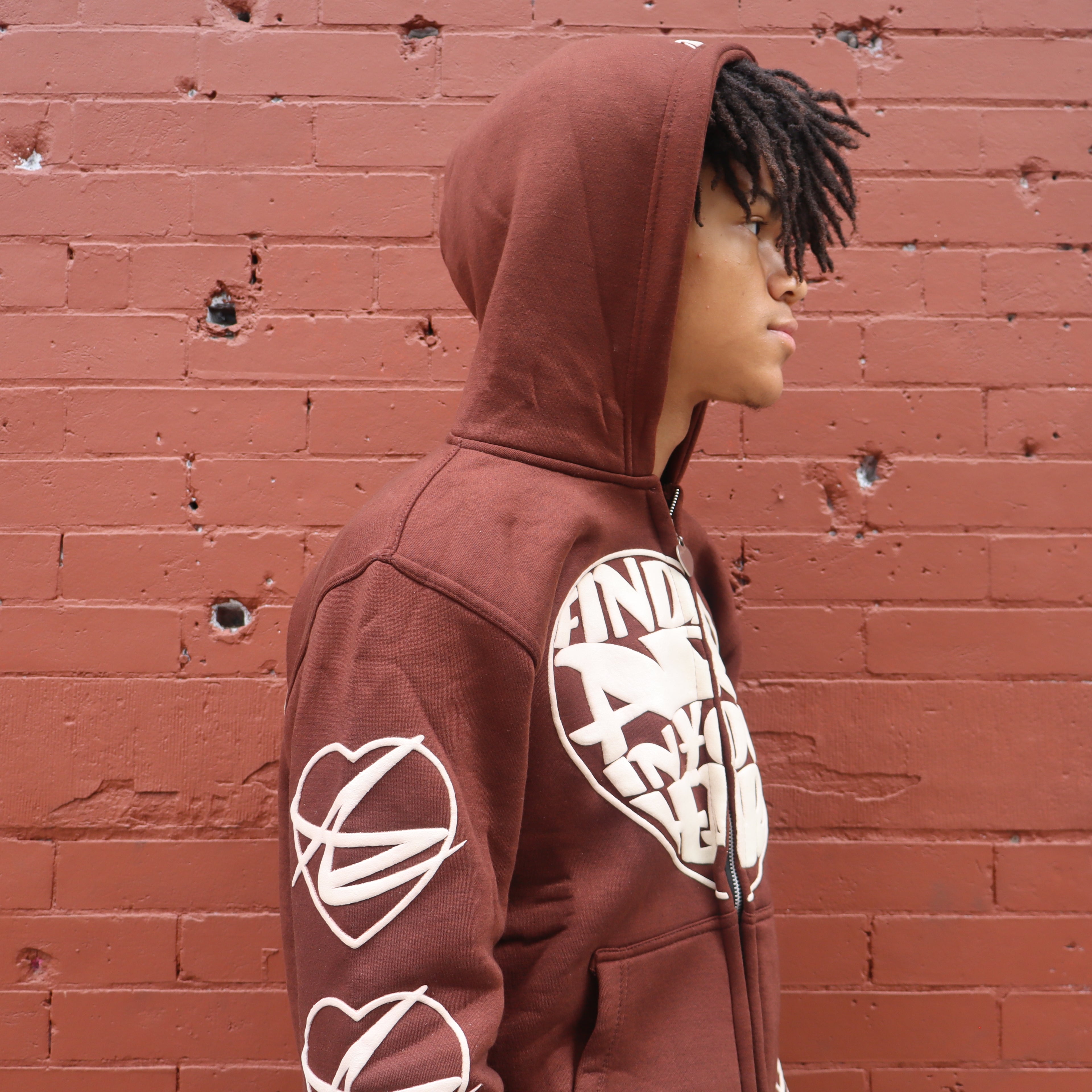 Person wearing a maroon hoodie with white graphics against a red brick wall
