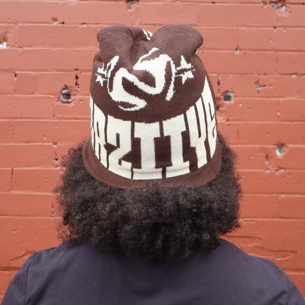 Person wearing a brown knit hat with white text against a red brick wall
