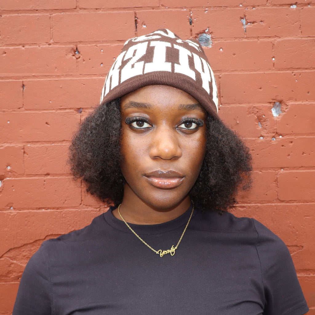 Person wearing a beanie and black shirt against a red brick wall